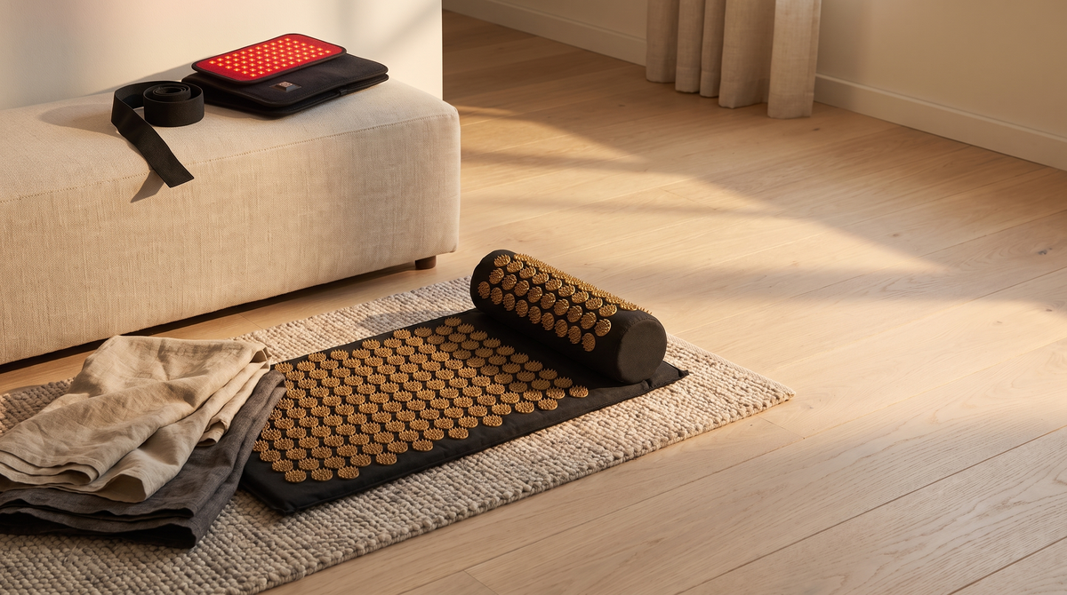 An acupressure mat and bolster on a rug, with a red light pad on a linen bench